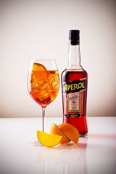 a bottle of aperol next to a glass filled with wine and orange peels