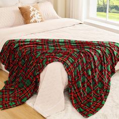 a bed with a red and green plaid blanket on top of it next to a window