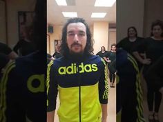 a man with long hair wearing a yellow and black shirt is standing in a hallway