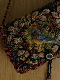 a bird is sitting on top of a purse with flowers and leaves around it's edges