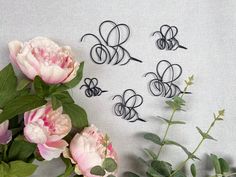 three metal scissors are sitting next to some pink flowers and green leaves on a white surface