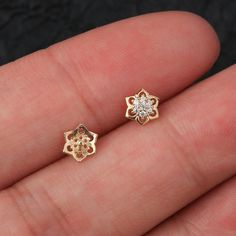 a person's hand holding two small gold and diamond earrings