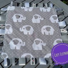 a gray and white elephant print baby blanket on a bench with ribbon around the edges