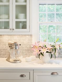 a kitchen with white cabinets and flowers on the counter top in front of a window