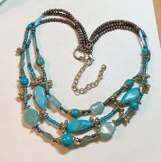 A bright and fresh vintage beaded necklace in blue and turquoise hues. The necklace is about 20 to 23 inches long.  Silvertone metal, with darker silvercolored beads.  Bright faux turquoise and blue plastic beads.  Also bugle beads and little Charlotte beads.  Lobster claw clasp.  Chain extender.  No stamps or marks.  Good vintage condition, with some surface wear, and some wear and discoloration to the metal. You can find more vintage necklaces here: https://www.etsy.com/shop/OtterCatHaus?section_id=17074037&ref=shopsection_leftnav_1&view_type=list Please convo with any questions.  I combine shipping, and refund overages of more than fifty cents.  Thanks for stopping by today. Blue Beaded Multi-strand Layered Necklace, Multi-strand Metal Beads Jewelry, Blue Multi-strand Beaded Layered Necklace, Adjustable Multi-strand Turquoise Beaded Necklace, Multi-strand Turquoise Gemstone Beads Necklace, Blue Multi-strand Jewelry With Dangling Beads, Adjustable Multi-strand Turquoise Blue Necklace, Blue Jewelry With Silver Metal Beads, Turquoise Bohemian Beaded Layered Necklace