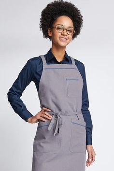 a woman wearing an apron and glasses standing with her hands on her hips, smiling at the camera