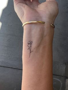 a woman's arm with a small flower tattoo on her left wrist and gold bracelet