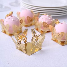 some pink and gold decorated desserts on a white table with plates in the background