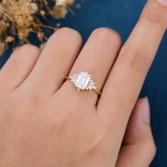 a woman's hand with a diamond ring on it and flowers in the background