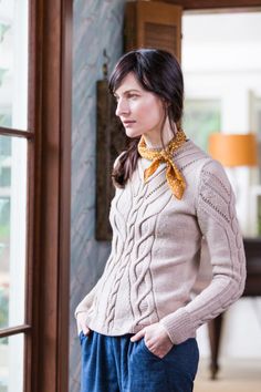 a woman standing in front of a window wearing a sweater