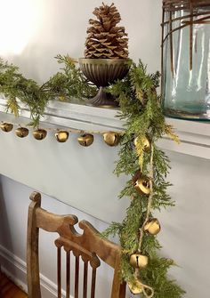 a wooden chair sitting next to a fireplace covered in pine cones and greenery with bells hanging from the mantle