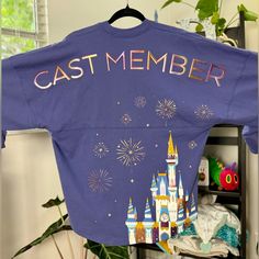 a purple shirt that says cast member hanging on a rack in front of a window