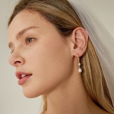 a woman wearing a veil and earrings with pearls on the side of her head is looking off into the distance