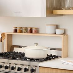 a stove top oven sitting inside of a kitchen next to a wooden shelf filled with glasses