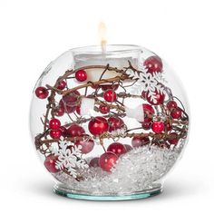 a candle that is inside of a glass bowl filled with snowflakes and berries