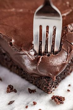 a fork stuck into a piece of chocolate cake with frosting on the top and bottom