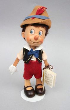 a doll with a hat and red pants holding a book in his hand, standing on a white base