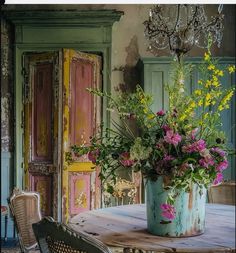 a vase with flowers sitting on top of a table next to a chair and door