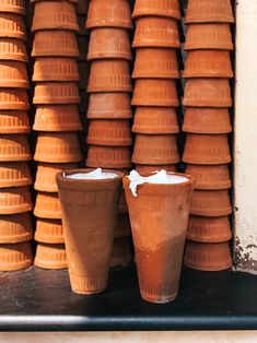 two cups sitting next to each other in front of stacks of clay pots