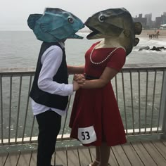 two people dressed in costumes standing on a pier near the ocean and holding hands with each other