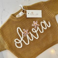 a sweater with the word love written in white thread and flowers on it next to a tag