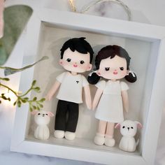 two dolls in a shadow box with a dog and cat