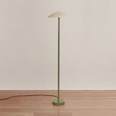 a green floor lamp with a white shade on the base and a black cord plugged into it