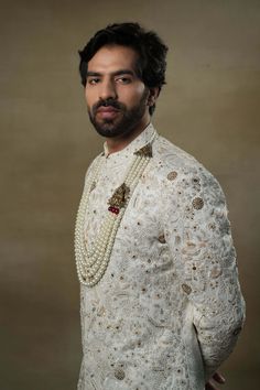 Editor's Note Featuring our work of art in our white all over hand-embroidered sherwani set. The foundation is crafted using machine embroidery adorned with tone on tone thread serving as the base texture, while the second tier showcases highlighting with 3D brass elements, dabka and zari threads. Fabric: Linen silk Color: Ivory, gold Components: Sherwani, kurta and churidar Occasion: Groom Fit: Regular Note: Product colour may slightly vary due to photographic lighting sources Care: Dry clean o Festive Designer Sets With Pearl Embroidery, Reception Sets With Naqshi In Traditional Drape, Gold Chikankari Embroidery Sets For Reception, Gold Sets With Chikankari Embroidery For Reception, Elegant Sherwani With Pearl Embroidery For Diwali, White Raw Silk Sets With Pearl Embroidery, Transitional Festive Kurta With Pearl Embroidery, Festive Off White Sets With Pearl Embroidery, Traditional Sherwani With Pearl Embroidery For Diwali