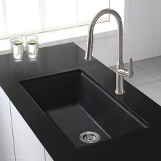 a black kitchen sink sitting under a window next to a faucet and two glasses