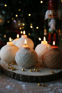 some white balls are sitting on a wooden plate with candles in front of a christmas tree