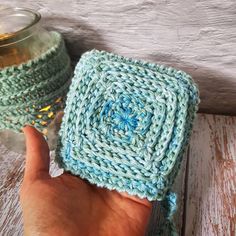 a hand is holding up a crocheted square in front of a mason jar