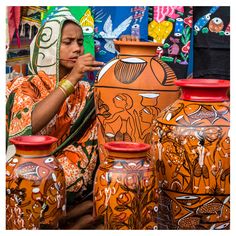 a woman sitting in front of some vases with designs on them and pointing to the side