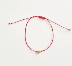 a red string bracelet with two gold hearts on it and a white beaded cord