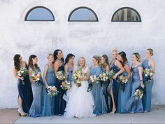 a group of women standing next to each other in front of a white wall holding bouquets