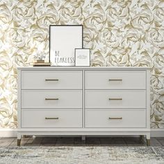 a white dresser sitting in front of a wall with a framed picture on top of it