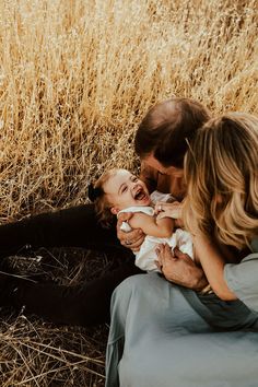 three adults and one baby are sitting in the grass with their hands around each other