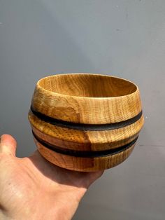 a hand holding a wooden bowl in front of a gray wall with black stripes on it