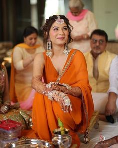 a woman in an orange sari sitting on the ground with other people around her