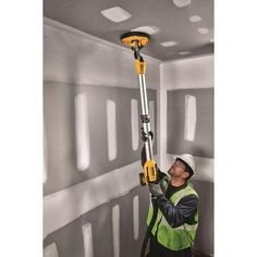 a man in a green vest is using a hand held drill to paint the walls