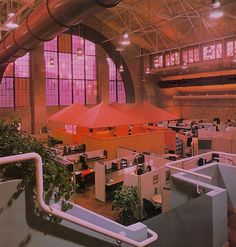 an office building with lots of cubicles and plants on the floor, in front of large windows