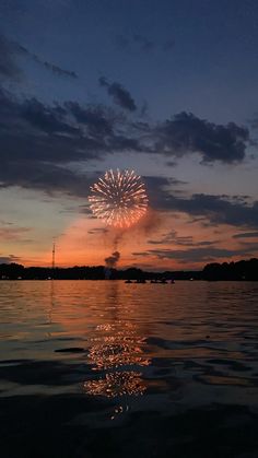 fireworks are lit up in the sky above water at sunset or dawn with reflection on surface