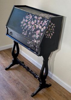 a black table with flowers painted on the top and bottom, sitting in front of a wall