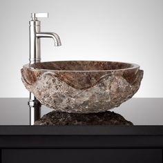 a bowl shaped stone sink on top of a black counter with a faucet