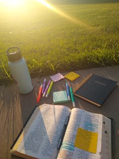 an open book sitting on top of a sidewalk next to a cup and some writing utensils