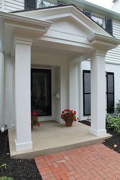 a white house with red flowers on the front door and brick walkway leading up to it