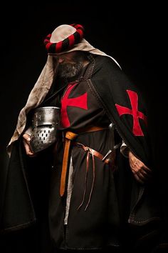 a man dressed in medieval clothing and holding a metal pot with a red cross on it