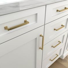 a white and gold kitchen with marble counter tops, brass handles and pulls on the cabinets