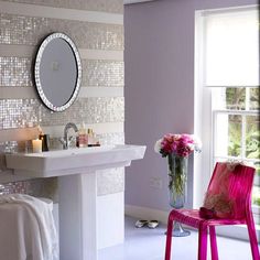 a pink chair sitting in front of a white sink next to a mirror on the wall