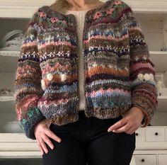 a woman standing in front of a white cabinet wearing a multicolored cardigan