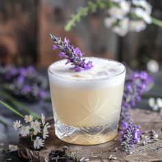 a drink with lavender sprigs on the rim sits on a piece of wood